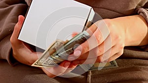 Woman hands holding white gift box with money, openning it and counting dollars during birthday holiday congratulations