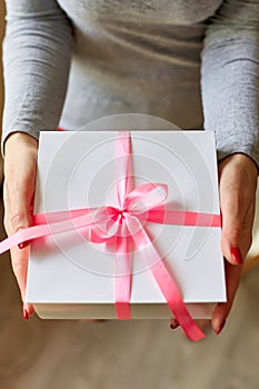 Woman hands holding a white present box with pink ribbon