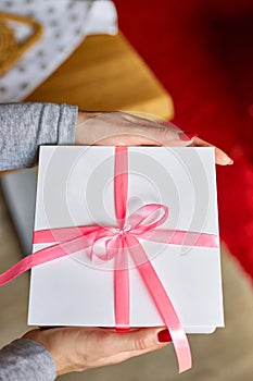 Woman hands holding a white present box with pink ribbon