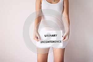 Woman hands holding a white sign with the word urinary incontinence on white background