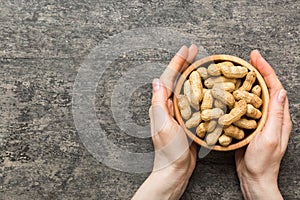 Woman hands holding a wooden bowl with close peanuts. Healthy food and snack. Vegetarian snacks of different nuts