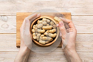 Woman hands holding a wooden bowl with close peanuts. Healthy food and snack. Vegetarian snacks of different nuts