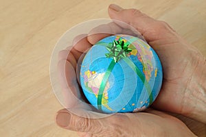 Woman hands holding the World with a green ribbon - Concept of protecting and saving the world; concept of the world as a gift