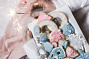 Woman hands holds a white plate with decorated winter/christmas cookies and a sparkle