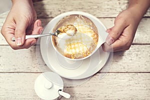 Woman hands with hot cappuccino coffee on a wood table.