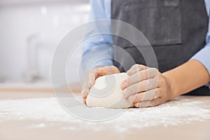 Woman hands kneading dough on board sprinkled with flour on background of light scandi kitchen