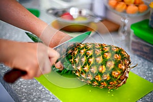 Woman hands with knife cutting pineapple top