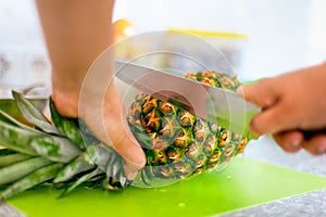 Woman hands with knife cutting pineapple top on cutting board