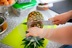 Woman hands with knife cutting pineapple top in domestic kitchen