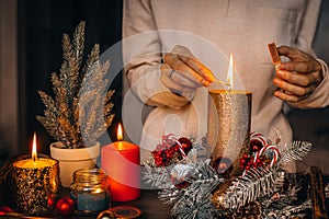 Woman hands lightning big gold candle with matches in Christmas wreath. Xmas interior decoration on rustic wooden background. hygg