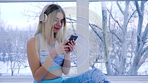 Woman with in hands listening to music through headphones on background of window