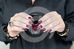 Woman hands with long nails and a bottle of dark red burgundy nail polish