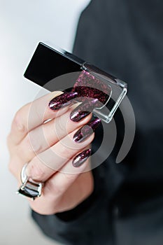 Woman hands with long nails and a bottle of dark red burgundy nail polish