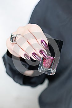 Woman hands with long nails and a bottle of dark red burgundy nail polish