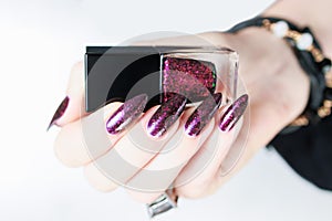 Woman hands with long nails and a bottle of dark red burgundy nail polish