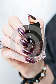 Woman hands with long nails and a bottle of dark red burgundy nail polish