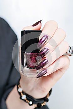 Woman hands with long nails and a bottle of dark red burgundy nail polish