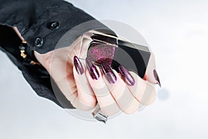 Woman hands with long nails and a bottle of dark red burgundy nail polish