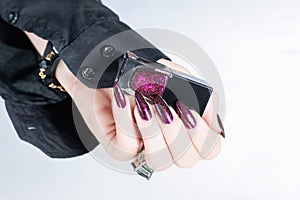 Woman hands with long nails and a bottle of dark red burgundy nail polish