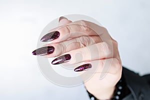 Woman hands with long nails and a bottle of dark red burgundy nail polish