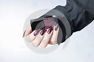 Woman hands with long nails and a bottle of dark red burgundy nail polish