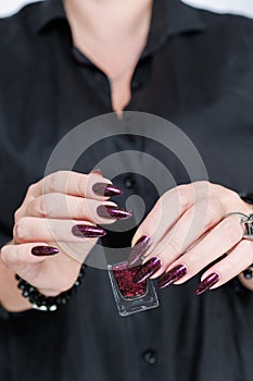 Woman hands with long nails and a bottle of dark red burgundy nail polish