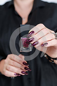 Woman hands with long nails and a bottle of dark red burgundy nail polish