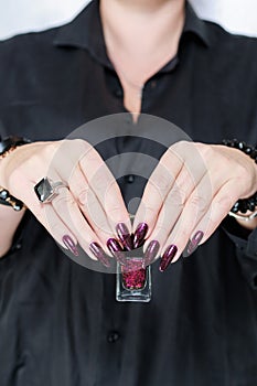 Woman hands with long nails and a bottle of dark red burgundy nail polish