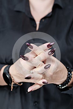 Woman hands with long nails and a bottle of dark red burgundy nail polish