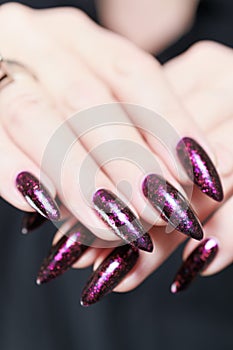 Woman hands with long nails and a bottle of dark red burgundy nail polish