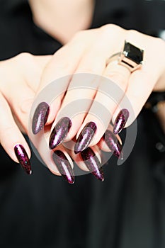 Woman hands with long nails and a bottle of dark red burgundy nail polish