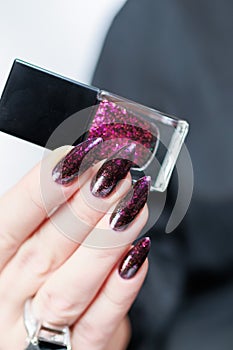 Woman hands with long nails and a bottle of dark red burgundy nail polish