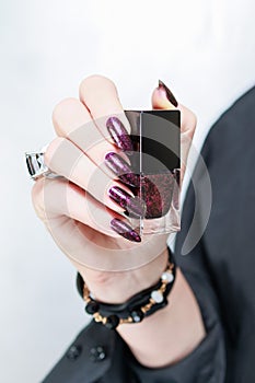 Woman hands with long nails and a bottle of dark red burgundy nail polish