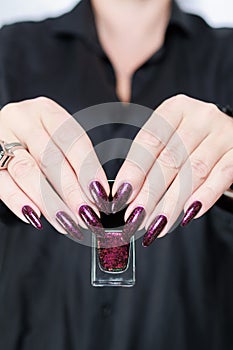 Woman hands with long nails and a bottle of dark red burgundy nail polish