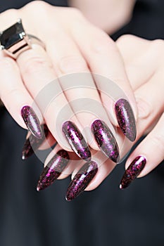 Woman hands with long nails and a bottle of dark red burgundy nail polish