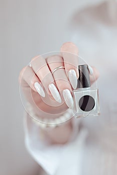Woman hands with long nails light white manicure and a bottle of nail polish