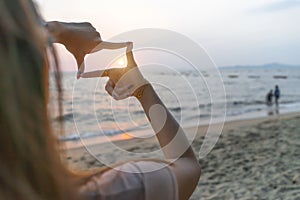 Woman hands making frame gesture distant with sunset on sea beach view, Female capturing sunlight outdoor. Future planning idea