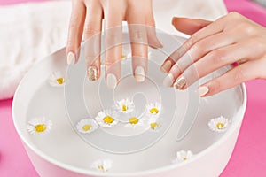 Woman hands with manicure nails and bowl with water and daisy flower