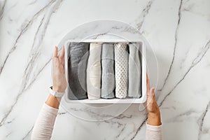 Woman hands neatly folding underwears and sorting in drawer organizers on white marble background.