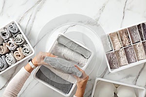 Woman hands neatly folding underwears and sorting in drawer organizers on white marble background.