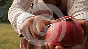 Woman hands opening fresh ripe pomegranate with knife on top of grass in countryside top view