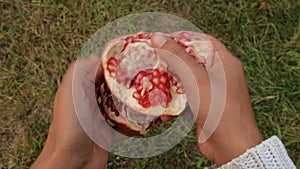 Woman hands opening fresh ripe pomegranate on top of grass in countryside top view