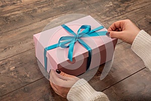 Woman hands opening gift box. Christmas, new year, birthday concept. Pink gift tied with blue ribbon, on wooden rustic table