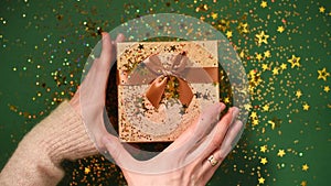 Woman hands opening gift box. Sparkling gold stars, glitter confetti over present. Unpacking gift on green background