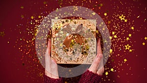 Woman hands opening gift box. Sparkling gold stars, glitter confetti over present. Unpacking gift on red background