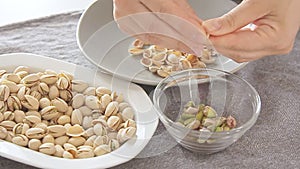 Woman hands opening pistachios above bowl