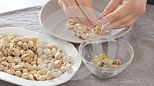 Woman hands opening pistachios above bowls