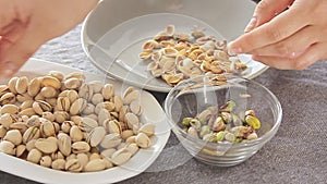 Woman hands opening pistachios above bowls