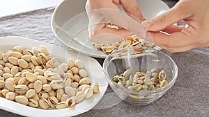 Woman hands opening pistachios above glass bowl