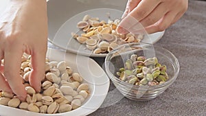 Woman hands opening pistachios above glass bowl